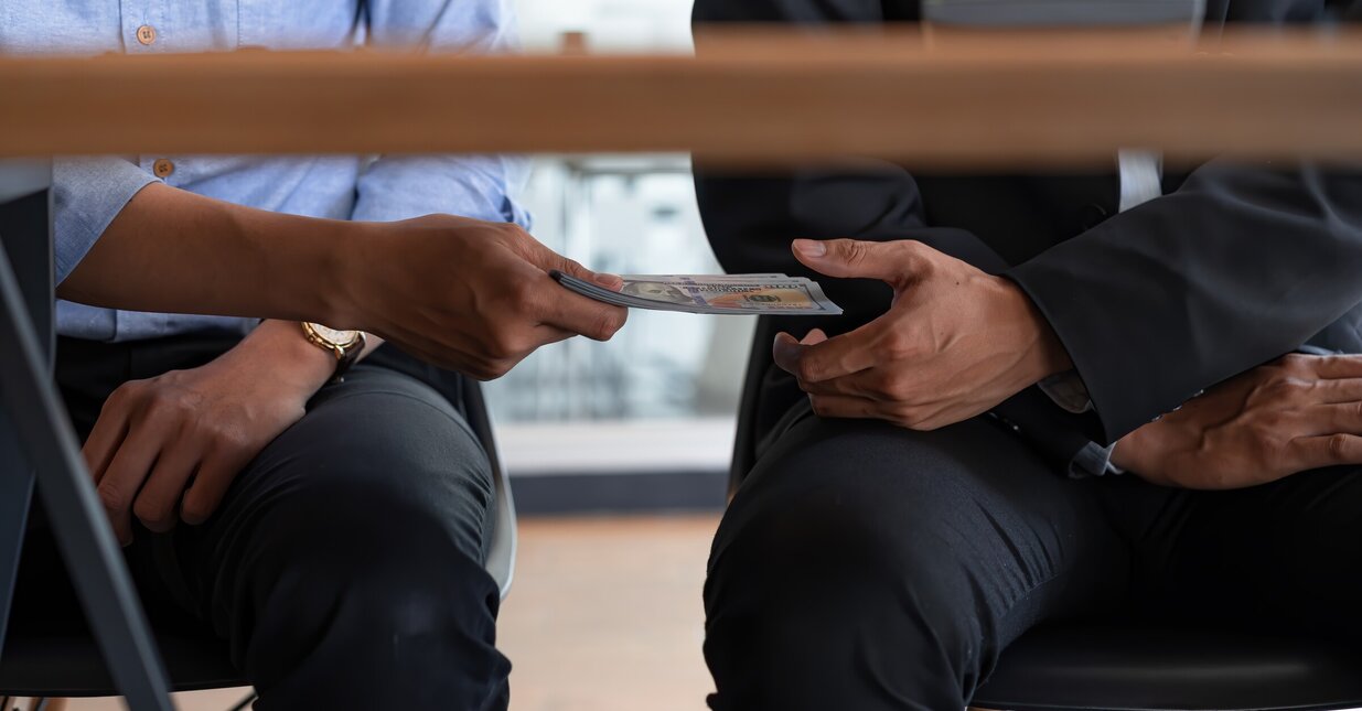 Pessoa a passar dinheiro sob a mesa