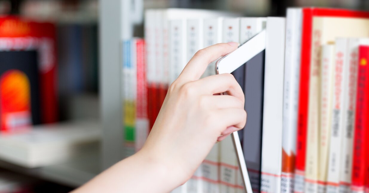 Pessoa a tirar tablet do meio de livros